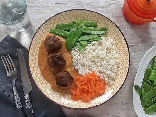 Fleischbällchen in Erdnuss-Kokos-Sauce mit Reis, Zuckerschoten und Möhrenrieb